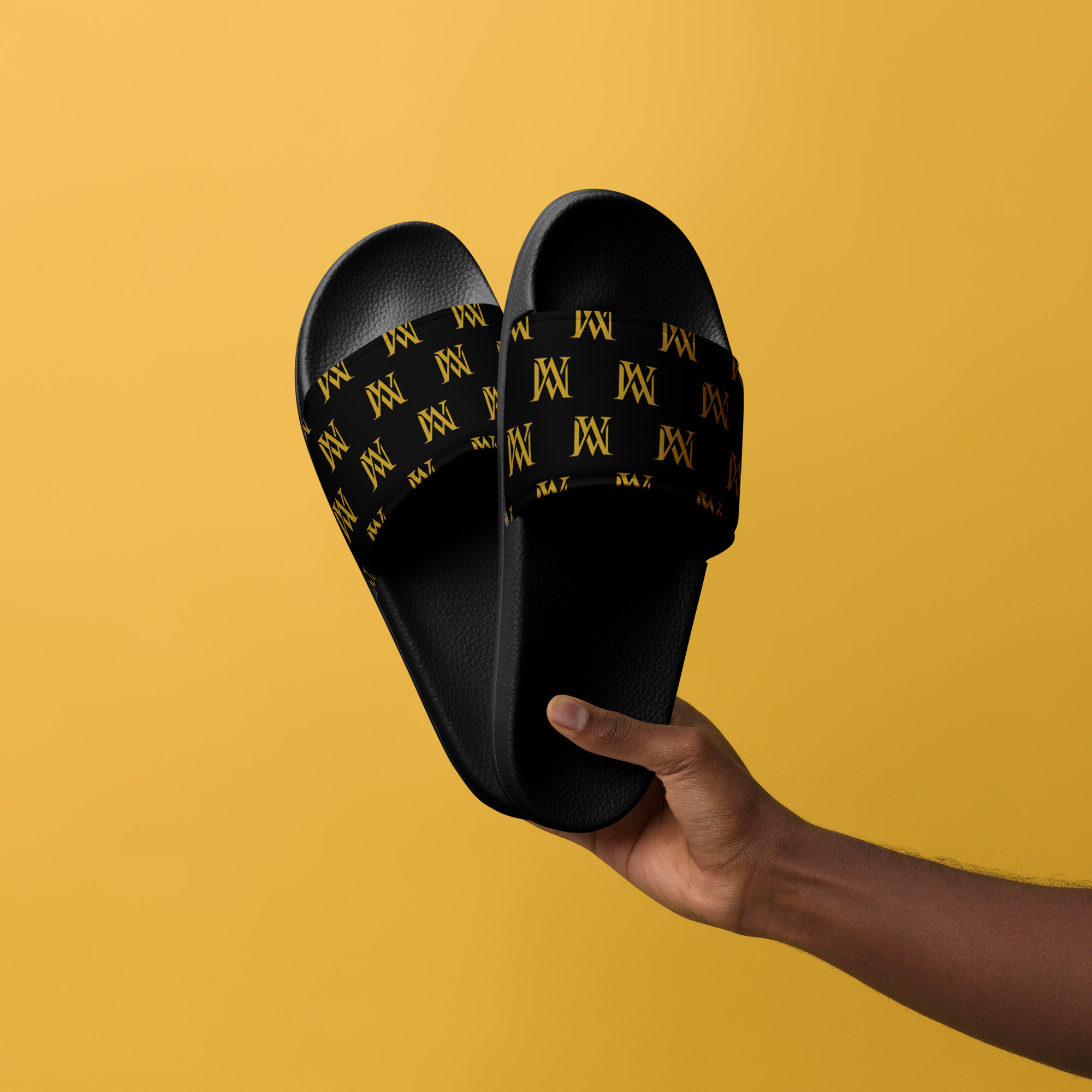Black monogram slide sandals held against yellow background