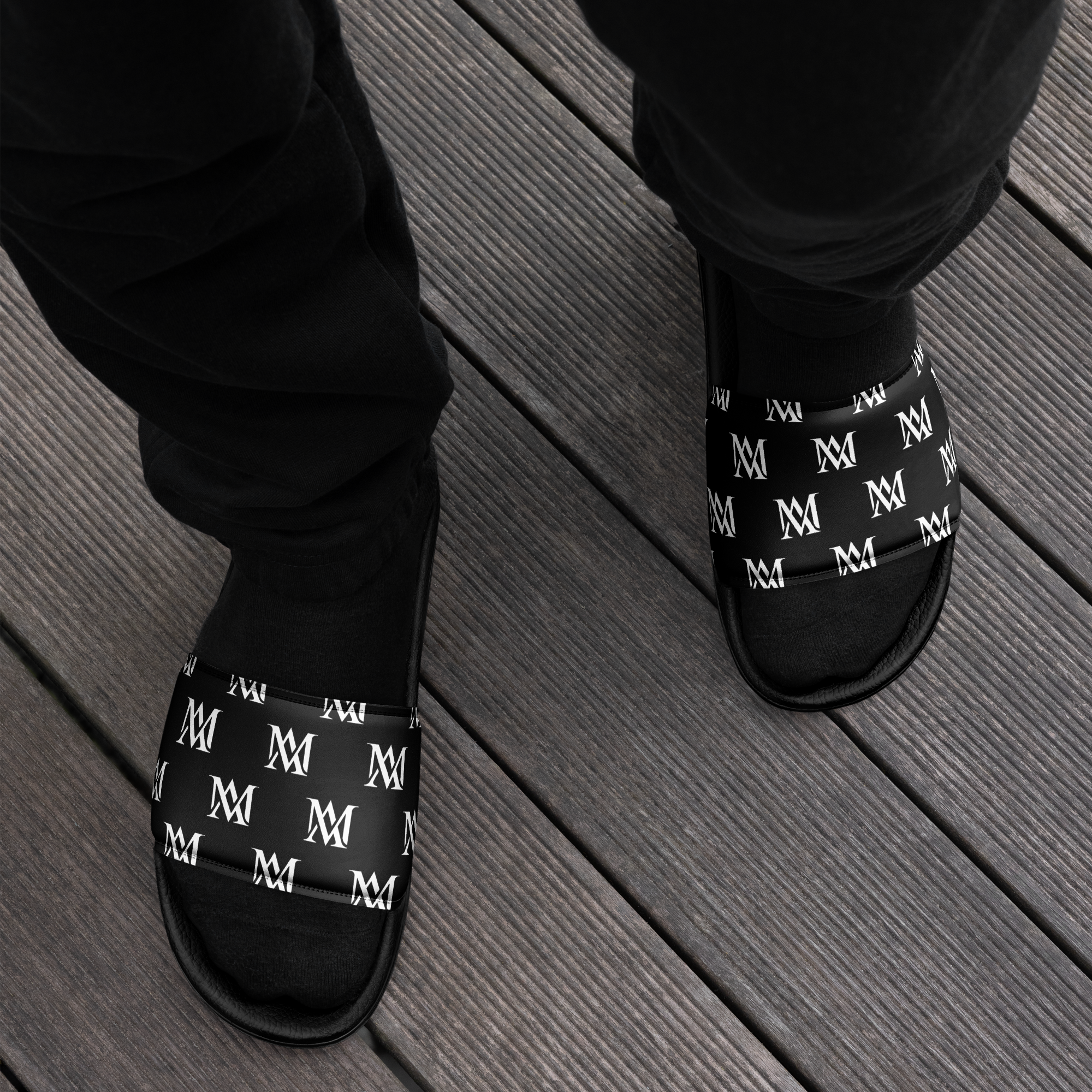 Person wearing black monogram slides on wooden deck